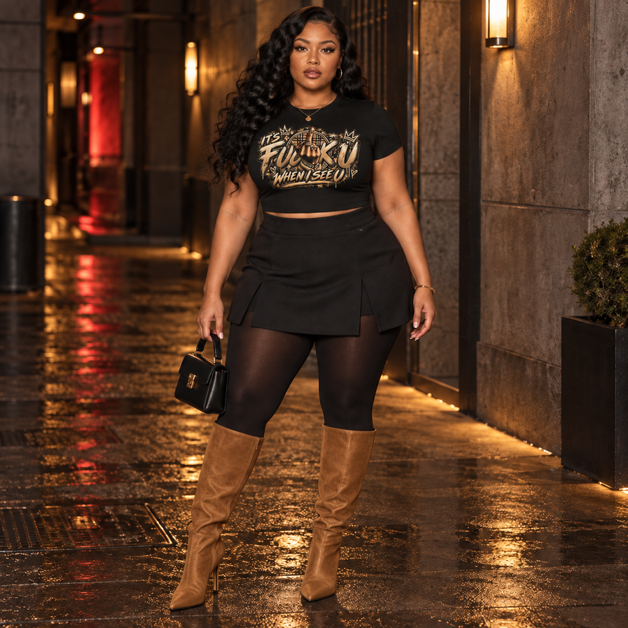 Female model front view wearing the black AnyWeather FUCK U WHEN I SEE U baby tee and caramel knee-high boots at night
